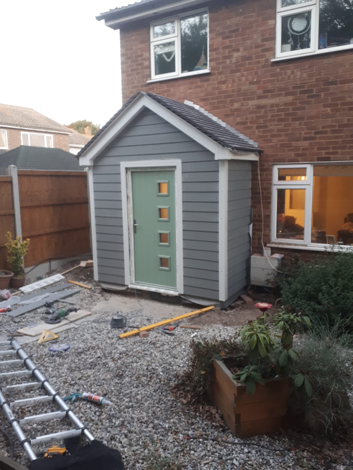New gabled porch with grey weatherboard cladding, white trims, a tiled roof and a sage green composite front door, nearing completion