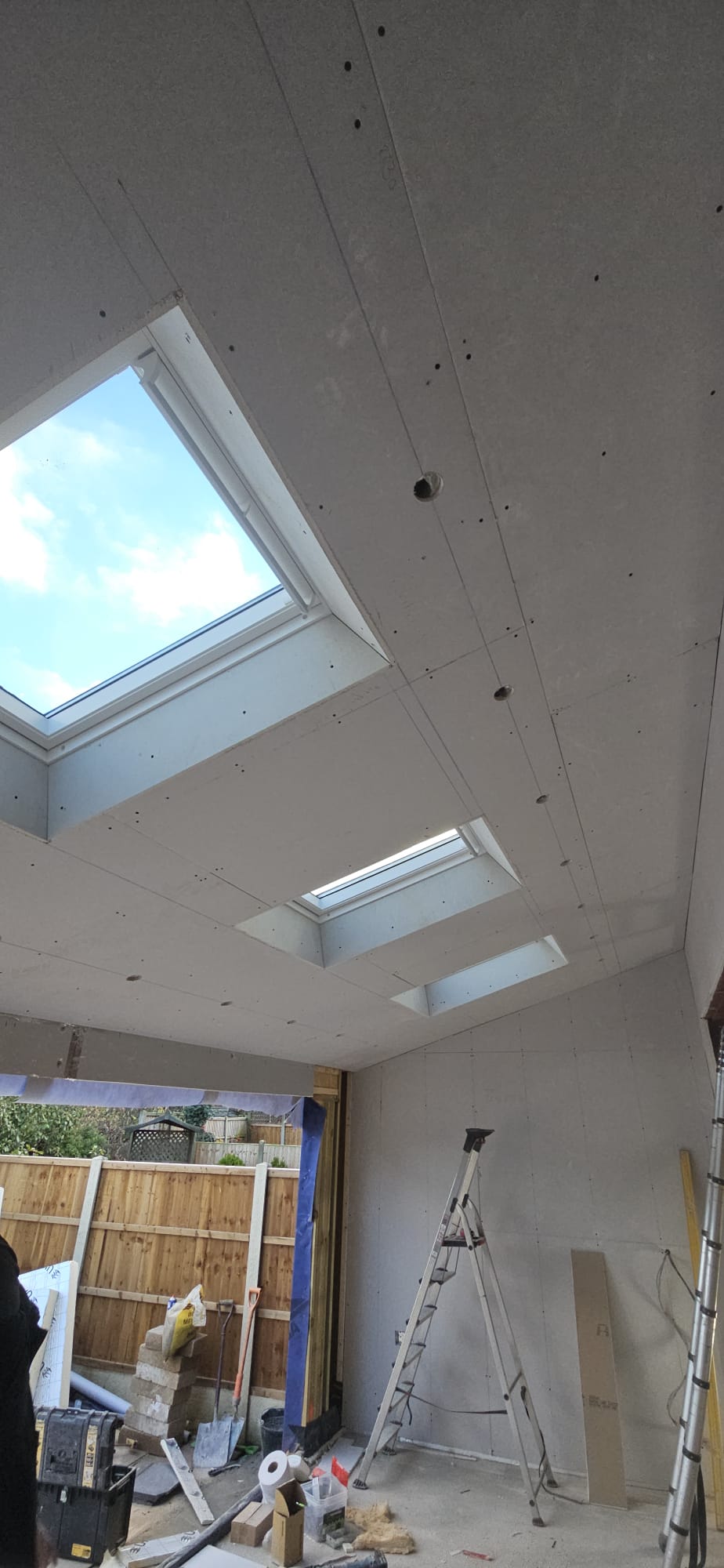 Plasterboarded sloping ceiling with three roof windows inside an extension under construction