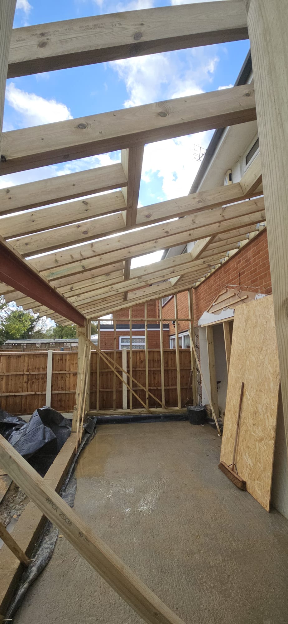 Looking up through the new timber rafters of a rear extension to a blue sky, with the stud wall frame and steel beam in place